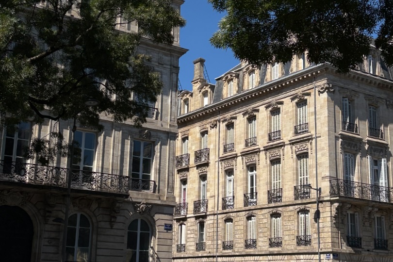 A limestone building in Bordeaux with trees and blue sky