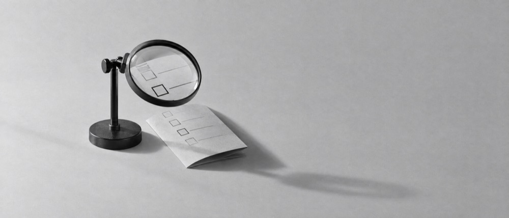 Photograph, greyscale: a folded paper ballot on a bare surface beneath a magnifying glass, nothing else in frame