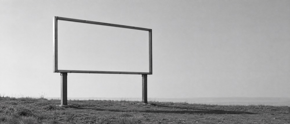 Photograph, greyscale: a large outdoor advertising hoarding on two posts against a blank sky, its frame completely bare