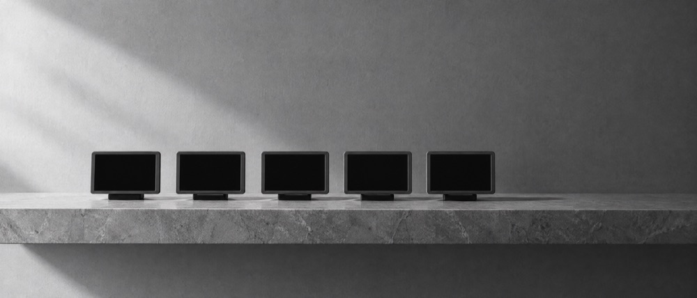 Photograph, greyscale: five small blank screens in a row on a stone shelf, every one dark and empty